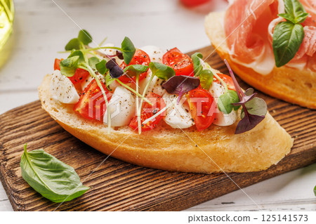 Tasty antipasto toasts featuring classic caprese with mozzarella and tomatoes, and savory prosciutto with herbs Tasty antipasto toasts featuring classic caprese with mozzarella and tomatoes, and savory prosciutto with herbs 125141573