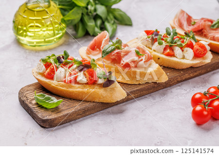 Tasty antipasto toasts featuring classic caprese with mozzarella and tomatoes, and savory prosciutto with herbs 125141574