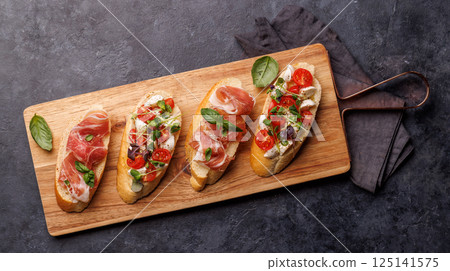 Tasty antipasto toasts featuring classic caprese with mozzarella and tomatoes, and savory prosciutto with herbs Tasty antipasto toasts featuring classic caprese with mozzarella and tomatoes, and savory prosciutto with herbs 125141575