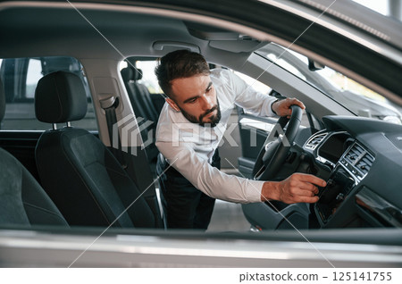 Examining the salon of the automobile. Young man in white clothes is in the car dealership 125141755