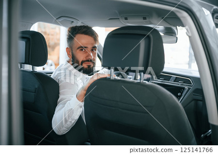 Looking behind. Young man in white clothes is in the car dealership 125141766