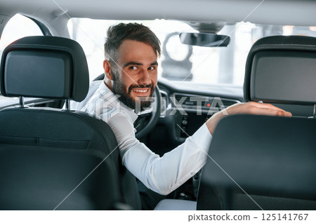 Looking behind. Young man in white clothes is in the car dealership Looking behind. Young man in white clothes is in the car dealership 125141767