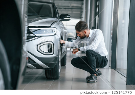 Checking the tires. Young man in white clothes is in the car dealership 125141770