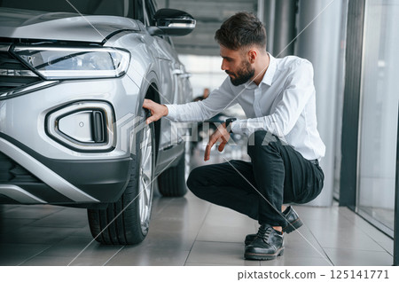 Checking the tires. Young man in white clothes is in the car dealership Checking the tires. Young man in white clothes is in the car dealership 125141771