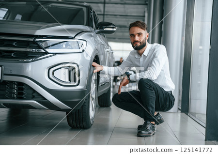 Checking the tires. Young man in white clothes is in the car dealership 125141772