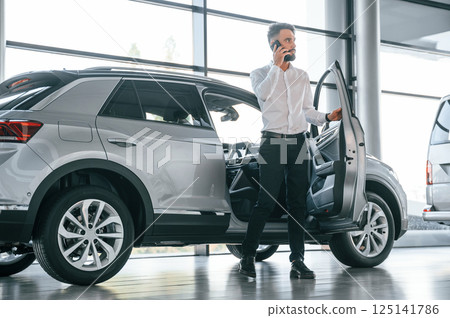 Walking out of automobile. Young man in white clothes is in the car dealership 125141786