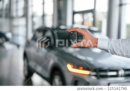 Closing the automobile by remote keys. Young man in white clothes is in the car dealership 125141790