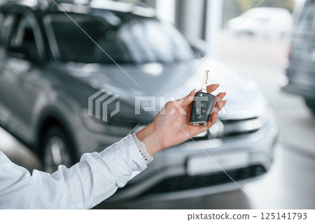 New owner holding keys. Young woman in white formal clothes is in the at dealership 125141793