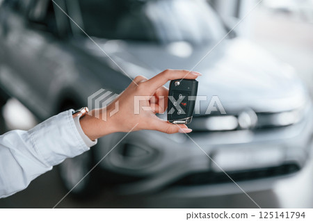 New owner holding keys. Young woman in white formal clothes is in the at dealership 125141794