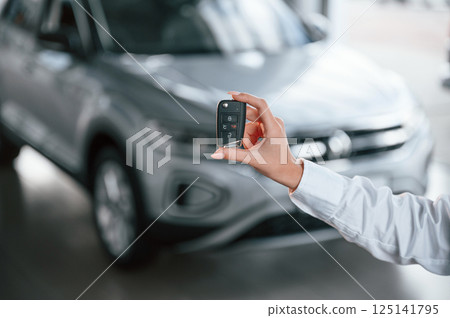 Close up view of keys. Young woman in white formal clothes is in the at dealership 125141795