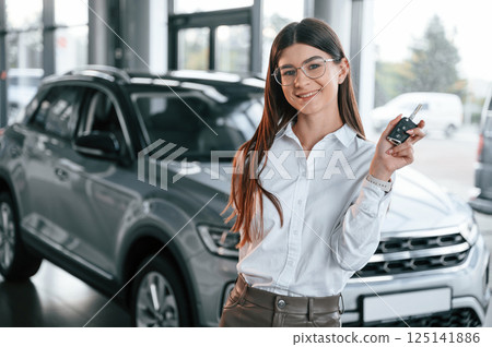 Holding keys. Young woman in white formal clothes is in the at dealership 125141886