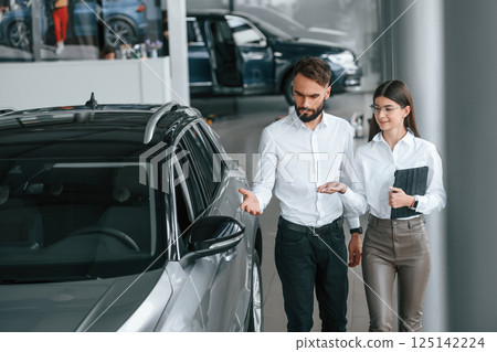 Walking and looking at the automobile. Man with woman in white clothes are in the car dealership together Walking and looking at the automobile. Man with woman in white clothes are in the car dealership together 125142224