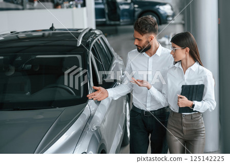 Walking and looking at the automobile. Man with woman in white clothes are in the car dealership together 125142225