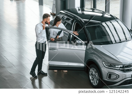 Door is opened. Man with woman in white clothes are in the car dealership together Door is opened. Man with woman in white clothes are in the car dealership together 125142245