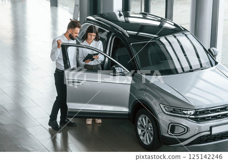 Door is opened. Man with woman in white clothes are in the car dealership together Door is opened. Man with woman in white clothes are in the car dealership together 125142246