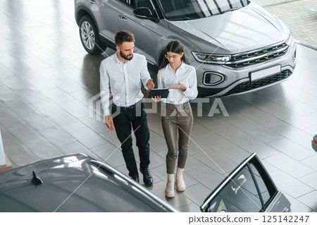 Top view. Man with woman in white clothes are in the car dealership together Top view. Man with woman in white clothes are in the car dealership together 125142247