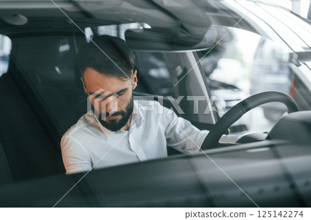Inside of the automobile. Young man in white clothes is in the car dealership Inside of the automobile. Young man in white clothes is in the car dealership 125142274