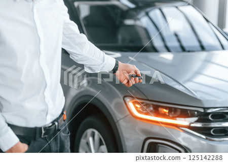 Using the keys remote controller. Young man in white clothes is in the car dealership Using the keys remote controller. Young man in white clothes is in the car dealership 125142288