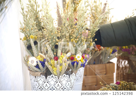 At an outdoor flower shop, ornamental bouquets of dried flowers and wheat are displayed. 125142398