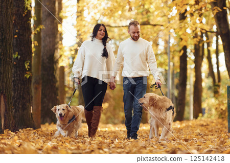Front view. Lovely couple are on the walk in autumn park with two dogs 125142418
