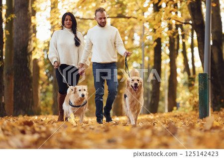 Lovely couple are on the walk in autumn park with two dogs Lovely couple are on the walk in autumn park with two dogs 125142423