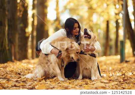Sitting on the ground and embracing the animals. Woman on the walk with her two dogs in the autumn forest 125142528