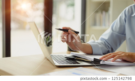 Businessman reviewing reports and working with laptop at desk 125142798