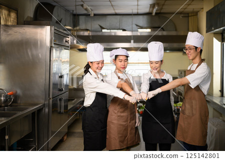 Group of students in uniform doing a group fist bump before starting their cooking session Group of students in uniform doing a group fist bump before starting their cooking session 125142801