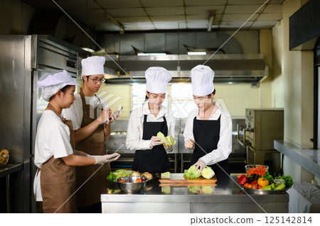 Group of culinary students in chef hats learning food preparation techniques Group of culinary students in chef hats learning food preparation techniques 125142814