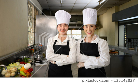 Confident culinary students in chef uniforms standing proudly in professional kitchen 125142827