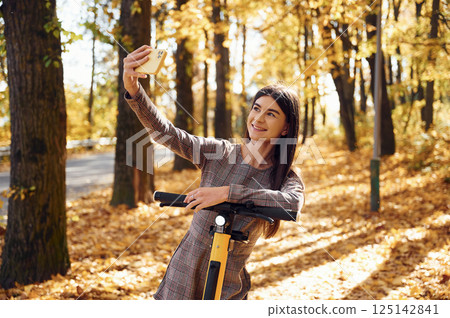 Young woman is making selfie by using smartphone while standing on the electric scooter 125142841