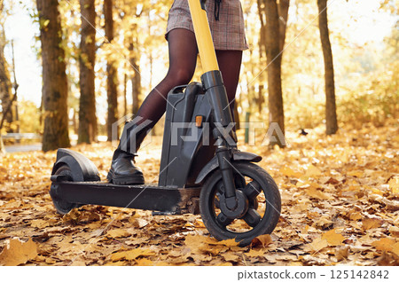 Close up view of woman's legs that are on the electric scooter in the forest at autumn season 125142842