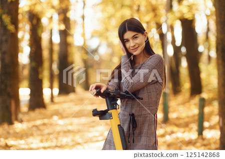 Young woman is riding electric scooter in the autumn forest 125142868
