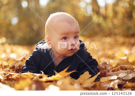 Cute little baby is lying down on the ground with fallen leaves on it 125143126