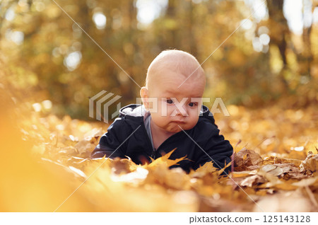 Cute little baby is lying down on the ground with fallen leaves on it 125143128