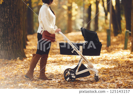 Mother with black colored pram is having a walk in forest at daytime Mother with black colored pram is having a walk in forest at daytime 125143157
