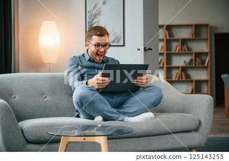 Celebrating success. Male freelance worker is using laptop at home. Cozy apartment 125143253