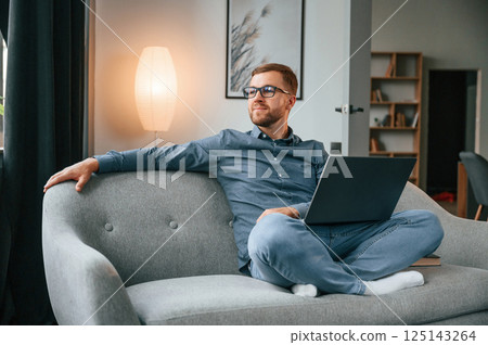 Sitting and looking at the side. Male freelance worker is using laptop at home. Cozy apartment 125143264