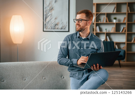 Sitting and looking at the side. Male freelance worker is using laptop at home. Cozy apartment 125143266