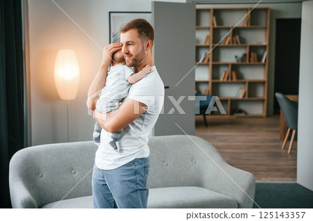 Holding baby in hands. Father with toddler is at home, taking care of his son Holding baby in hands. Father with toddler is at home, taking care of his son 125143357