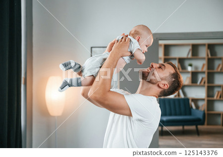 Smiling, having fun with baby is in the hands. Father with toddler is at home, taking care of his son 125143376