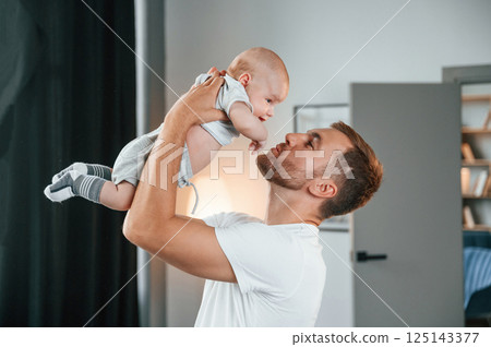 With baby in hands. Smiling, having fun. Father with toddler is at home, taking care of his son 125143377