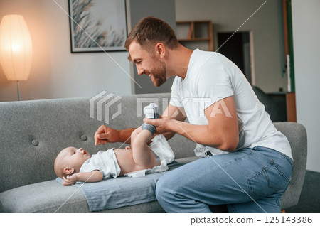 Father with toddler is at home, taking care of his son. Changing diapers Father with toddler is at home, taking care of his son. Changing diapers 125143386