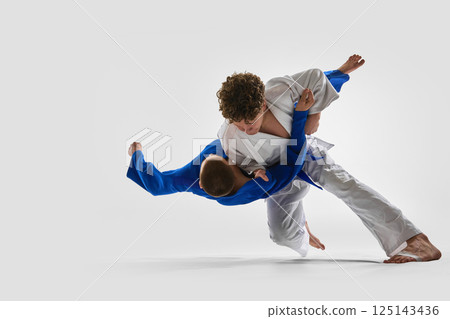 Dynamic mid-air twist as fighter in white unbalances opponent with strong stance, illustrating confidence, power against white background. Dynamic mid-air twist as fighter in white unbalances opponent with strong stance, illustrating confidence, power against white background. 125143436