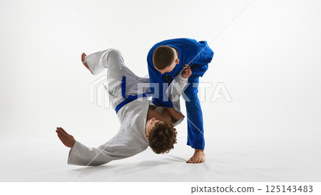Decisive hip throw unfolding, white gi athlete launches opponent in controlled arc, embodying skill against white background. Decisive hip throw unfolding, white gi athlete launches opponent in controlled arc, embodying skill against white background. 125143483