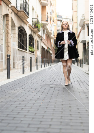 Happy woman in stylish dress walks along cobblestone street Happy woman in stylish dress walks along cobblestone street 125143491