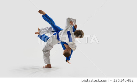 Energetic photo of judoka in white executes full-body rotation throw, opponent elevated off ground, representing precision against white background. Energetic photo of judoka in white executes full-body rotation throw, opponent elevated off ground, representing precision against white background. 125143492
