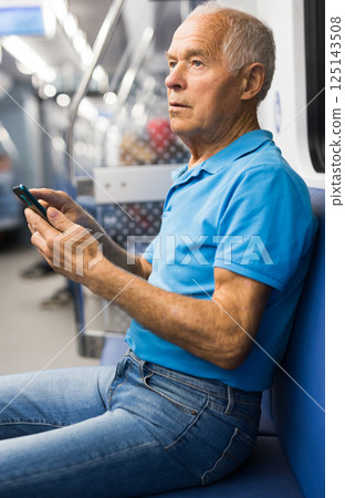 Old man sitting in subway car with smartphone Old man sitting in subway car with smartphone 125143508