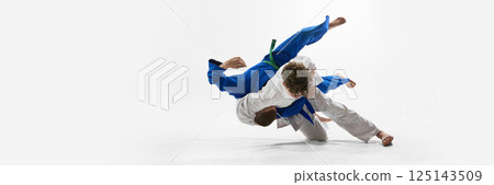 One competitor airborne with legs extended as opponent twists downward, expressing raw physical power, control against white background. One competitor airborne with legs extended as opponent twists downward, expressing raw physical power, control against white background. 125143509