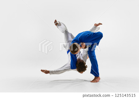 Judoka in blue performs dynamic shoulder throw, lifting opponent off ground in flawless arc, embodying technical excellence in martial arts tournament. 125143515